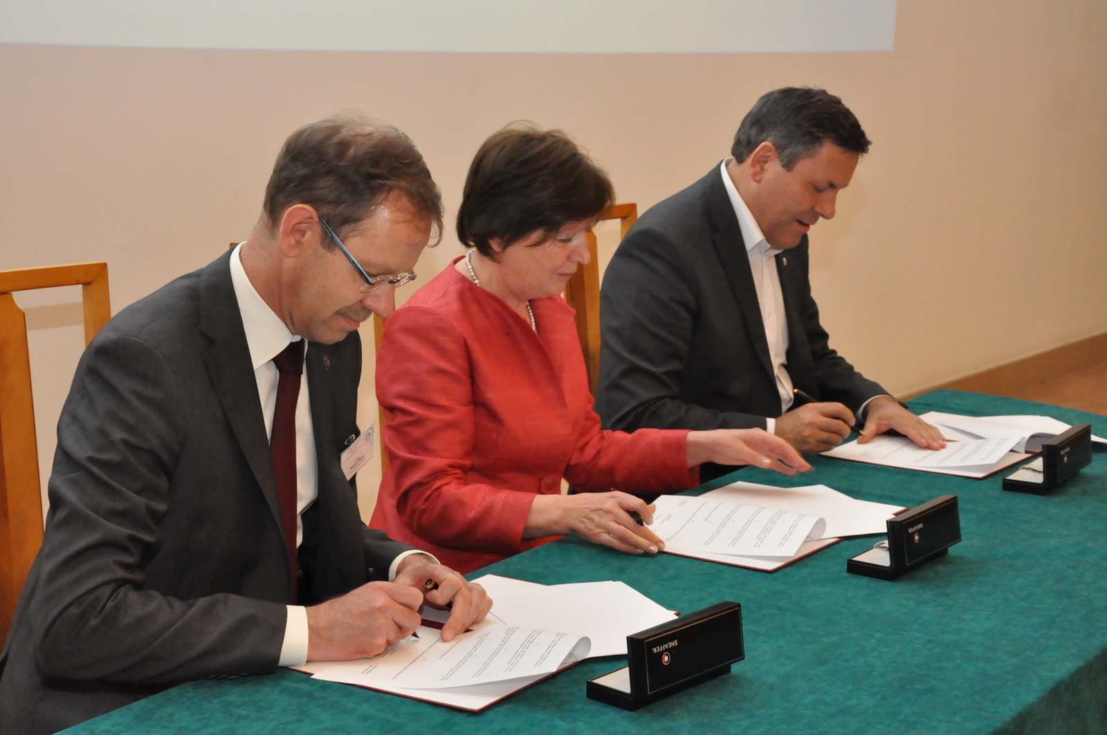 Podpisanie porozumienia o współpracy podczas jubileuszu 95-lecia GUM: Troje elegancko ubranych ludzi (dwóch mężczyzn i kobieta) siedzi przy stole i podpisuje dokumenty. 