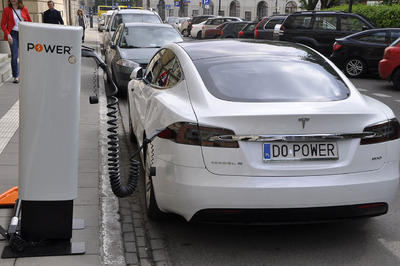 Samochód Tesla w trakcie ładowania Samochód Tesla stoi przy chodniku, podłączony do ładowarki pojazdów elektrycznych.