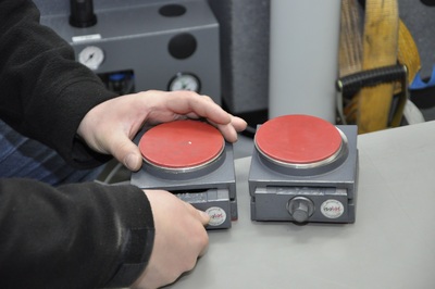  Widoczne są dwie ręce trzymające dwa nieduże przedmioty o kwadratowej podstawie i okrągłych, czerwonych wykończeniach, przypominających palniki elektryczne.