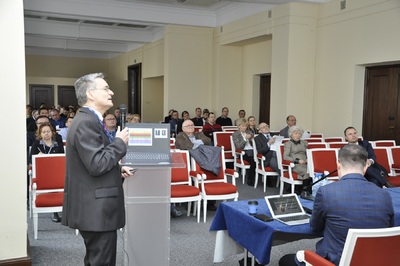  Widok sali konferencyjnej, na której siedzi kilkadziesiąt osób. Na pierwszym planie mężczyzna trzyma w ręku mikrofon. Stoi przy mównicy, na której leży laptop.