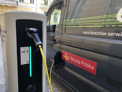  Ładowarka do pojazdów elektrycznych podłączona do ciemnego samochodu Poczty Polskiej.