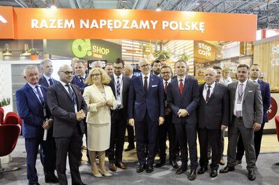  Kilkunastu elegancko ubranych mężczyzn i kobieta pozują do zdjęcia. Nad nimi napis Razem napędzamy Polskę.
