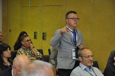 Profesor Tadeusz Szumiata - ekspert GUM Profesor Tadeusz Szumiata - ekspert GUM zabiera głos podczas dyskusji - mężczyzna w szarej marynarce i w okularach stoi pośród innych, siedzących osób, gestykuluje.