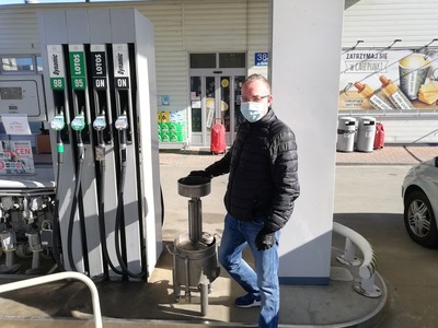 Legalizacja dystrybutorów na stacji paliw Mężczyzna w czarnej kurtce, dżinsowych spodniach i z białą maseczką na twarzy stoi przy dystrybutorze na stacji paliw.