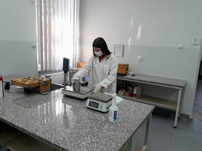 Legalizacja wag nieautomatycznych w Siedlcach Kobieta w białym fartuchu, z maseczką na twarzy dokonuje pomiaru odważnika na wadze w pomieszczeniu laboratoryjnym.