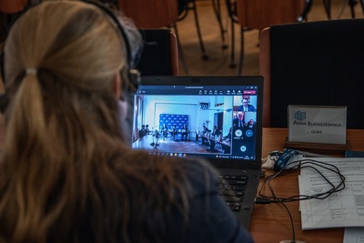 Głowa kobiety pochylona nad laptopem, na którym widać relację z oficjalnego spotkania.