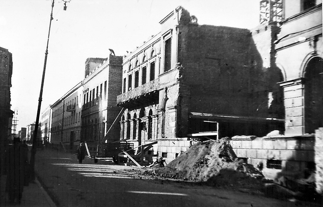 Czarno-białe zdjęcie z lat 40. Zrujnowany budynek GUM przy ulicy Elektoralnej. Część ruin leży na ulicy.. 