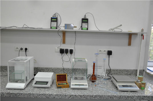 Fragment stanowiska pomiarowego do wzorcowania – wyznaczania pojemności statycznej w zakresie od 0,5 ml do 5000 ml; różne przyrządy stoją na blacie w laboratorium.
